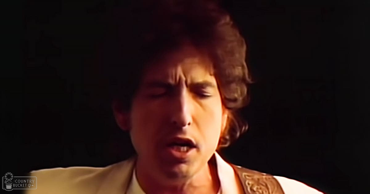 A young adult male singing indoors under dim lighting.