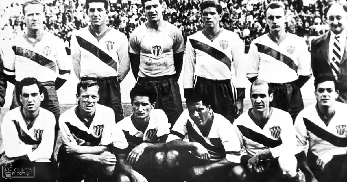 Historical soccer team photo from mid-20th century, seated players wearing white jerseys with black and red stripes across chest, dark shorts; standing players in similar attire, middle-aged man in suit jacket at back right, setting appears formal and possibly ceremonial.