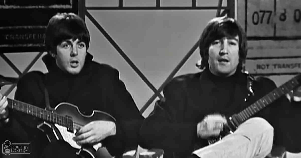 Indoor musical performance scene with two young adult males wearing dark-colored turtleneck sweaters; large window with metal frames in the background, suggesting a studio or warehouse setting.