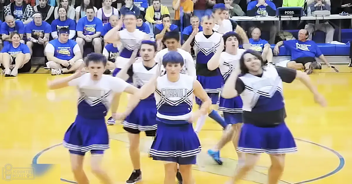Cheerleaders performing at an indoor sports arena with spectators in the background, wearing blue and white cheerleading uniforms.