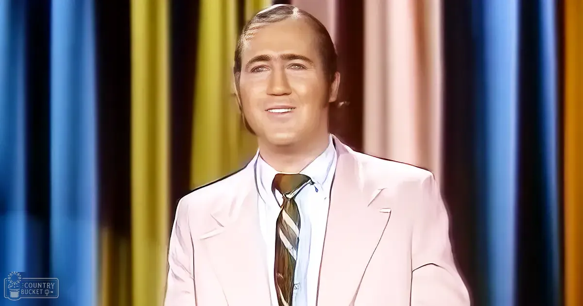 Adult male in a light pink suit jacket with a striped tie on stage against a backdrop of colorful curtains.