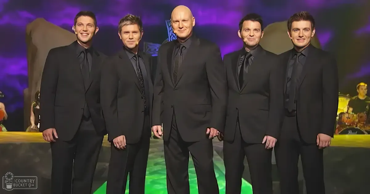 An indoor performance venue with a group of adult males dressed formally, possibly during an evening event. Stage lighting includes purple hues.