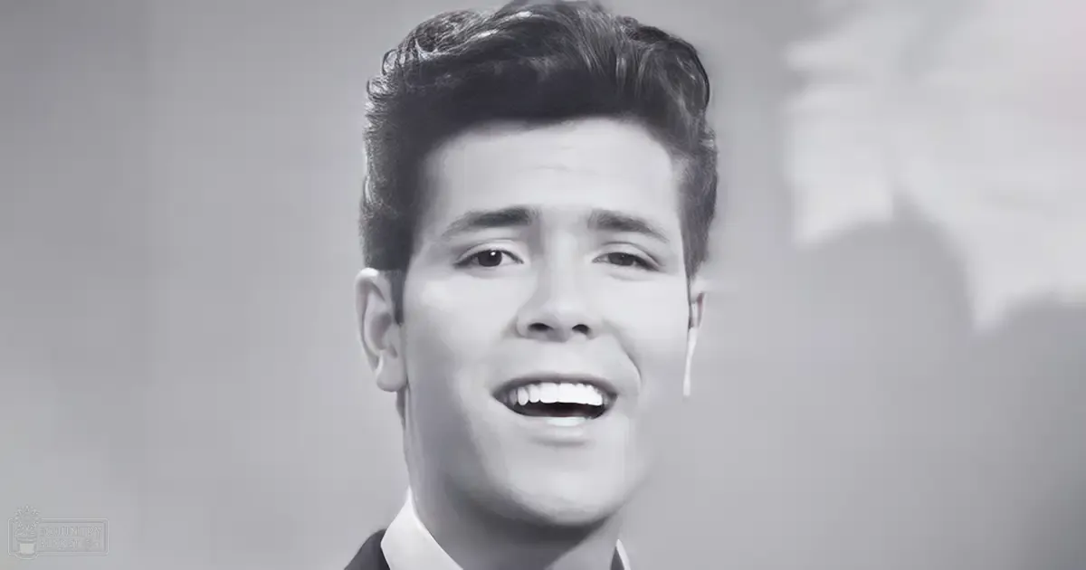 A young adult male with a mid-20th-century hairstyle wearing a formal shirt indoors.