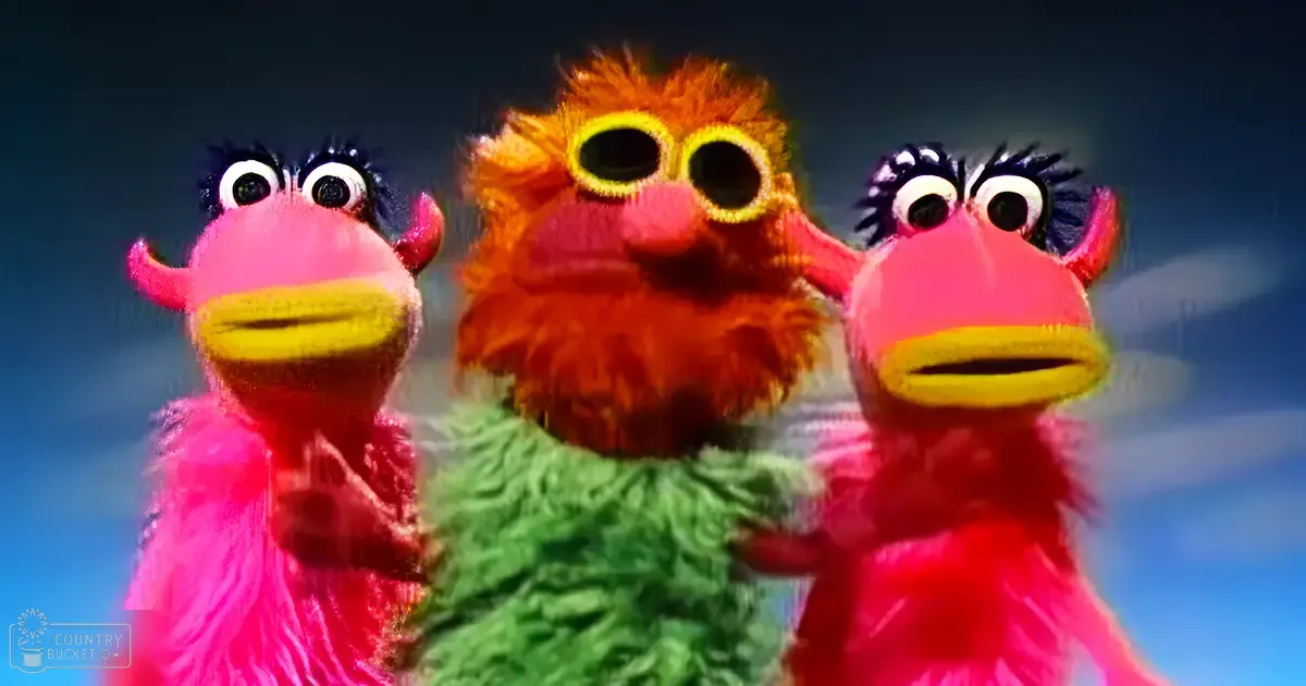Three puppet characters resembling birds with pink, green, and orange hues against a blue sky backdrop.