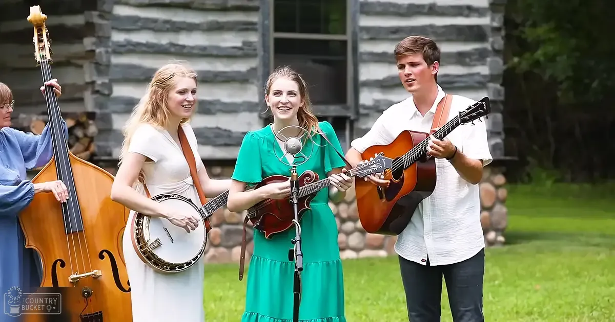 Musical performance in an outdoor setting with grass and stone building; people wearing casual cotton or linen garments; spring or summer ambiance.