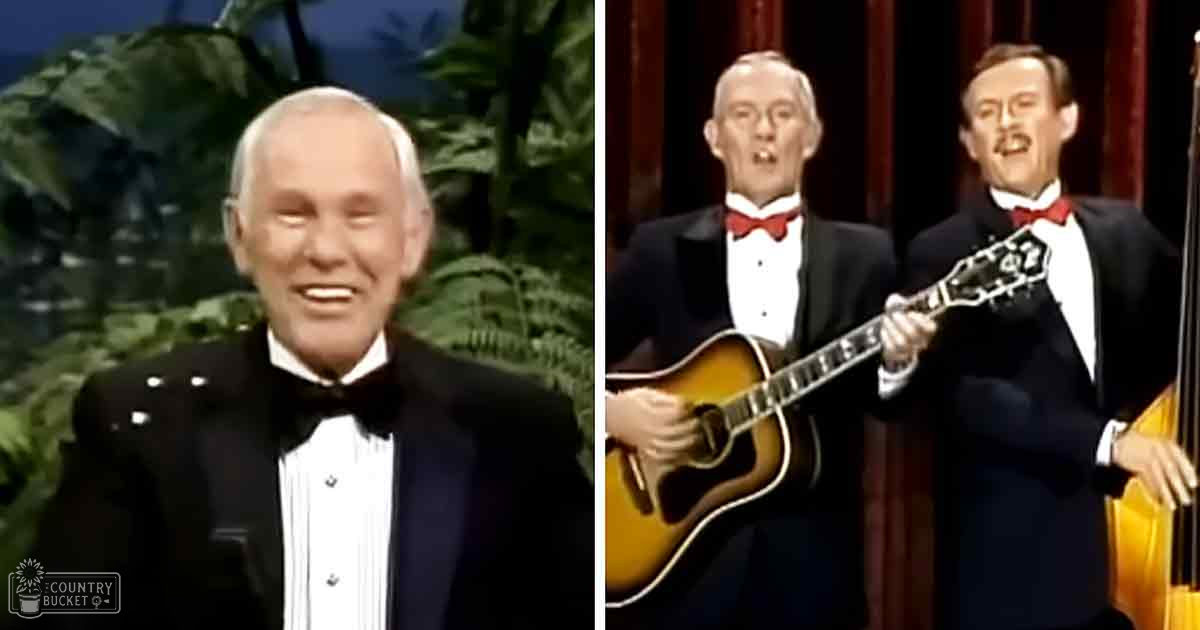 Three performers in formal tuxedos holding musical instruments on a stage with tropical greenery backdrop, likely from an indoor television production.