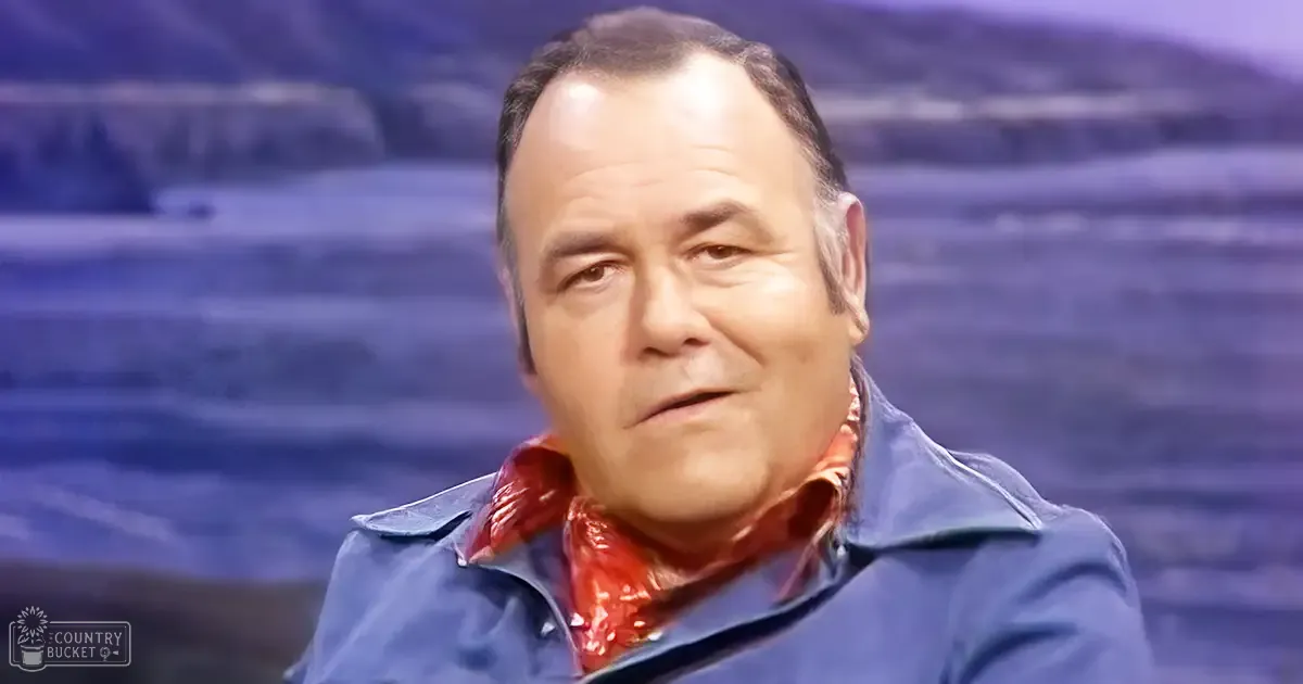 A middle-aged to older adult male in a stadium setting wearing a blue jacket with red patterned scarf, suggesting a casual yet stylish appearance.