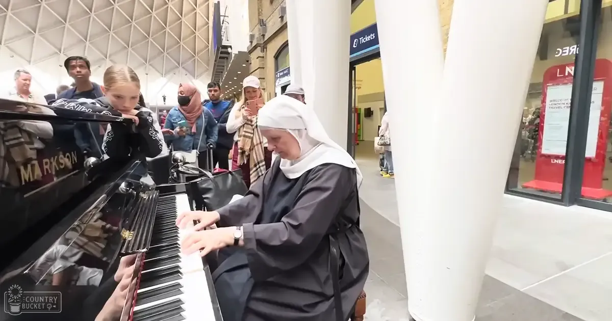 A nun playing piano amidst a bustling train station with various passengers and children around her.