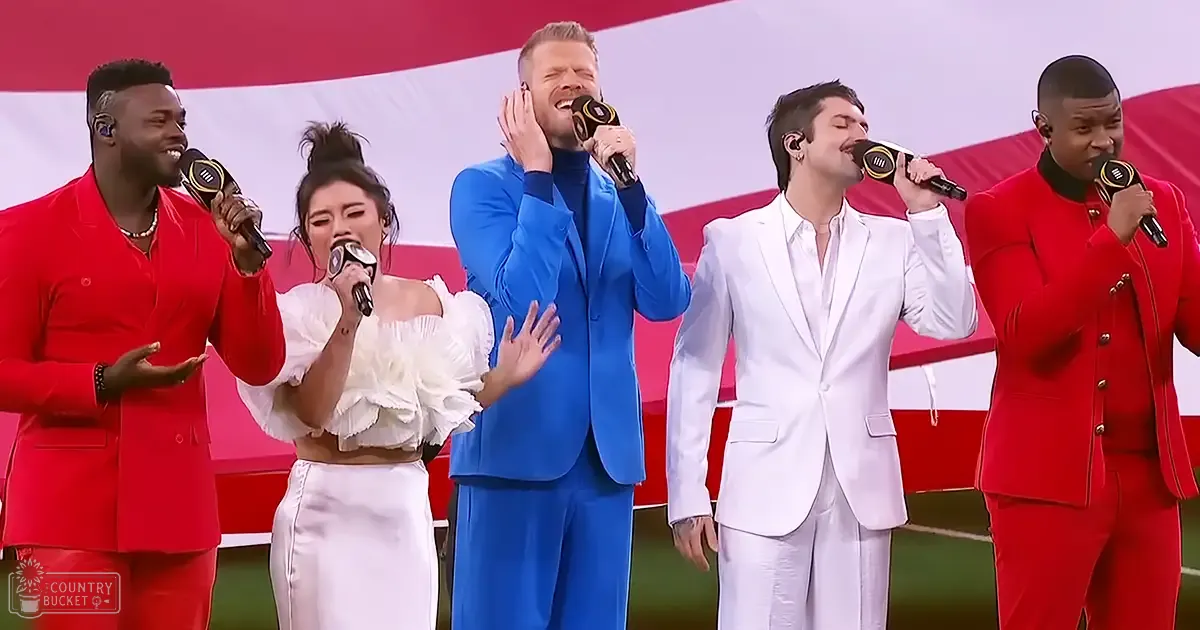 A group performance at an outdoor event with clear daylight conditions; American flag visible in the background.