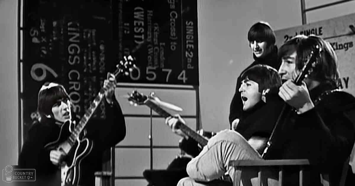 Four young adult males performing indoors, possibly in a recording studio or rehearsal space; seated individuals hold microphones while standing one holds a guitar.