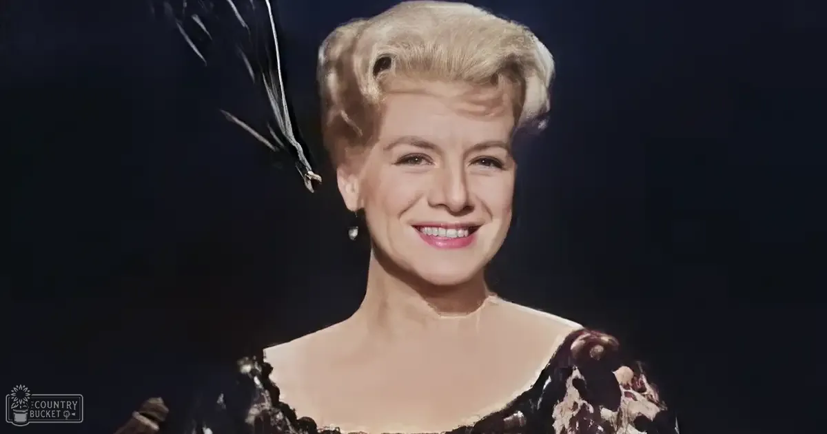 A middle-aged female wearing a dark, floral-patterned dress with short sleeves in an indoor setting with dim lighting.