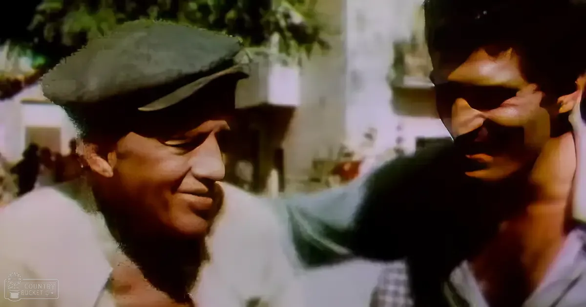 Two middle-aged men interact in a traditional outdoor setting with greenery and decorative elements, suggesting daytime sunlight.
