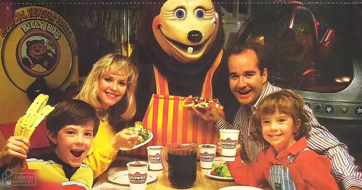 Family dining at Showbiz Pizza Place with Billy Bob Bear mascot, with a child in red and yellow striped shirt, adult female in yellow top, middle-aged male in striped button-up shirt, and another child in orange jacket and denim overalls. The setting includes white tableware, salads, pizza slices, and themed signage.