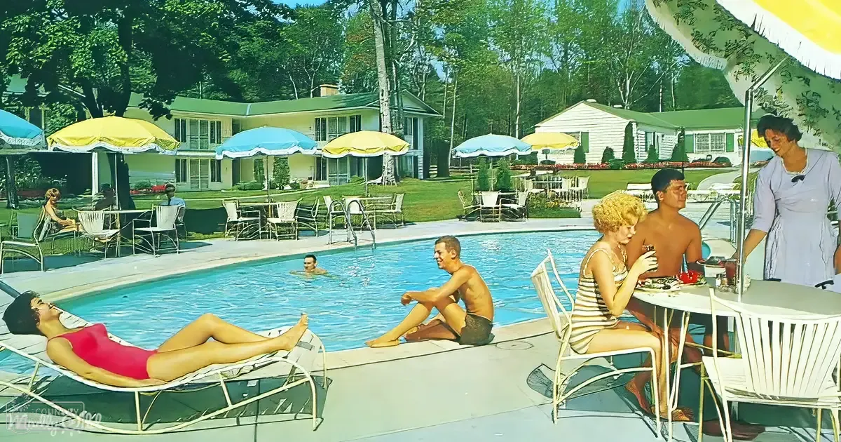 A vibrant poolside scene at a resort or vacation home with people enjoying summer attire. The setting is surrounded by trees and greenery under clear daylight.