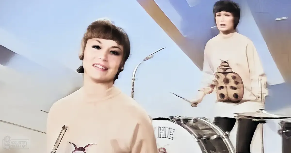 A young adult female in an urban setting wearing a light beige turtleneck sweater with a ladybug graphic, while another young adult male stands nearby in similar attire.