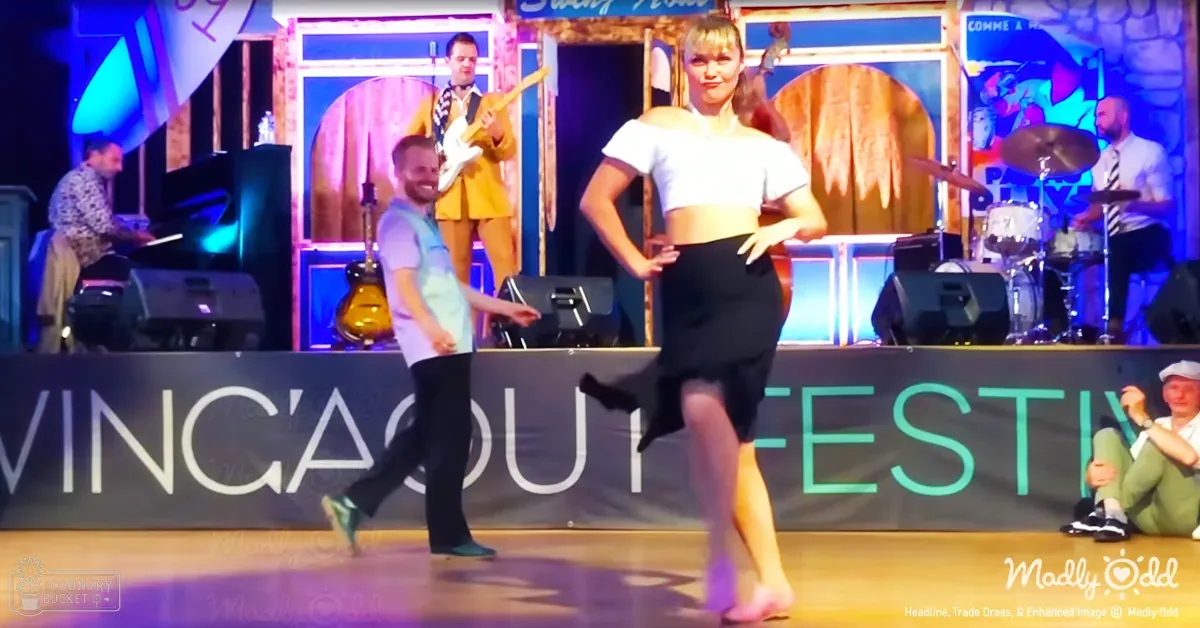 Young adult female dancer performing at Wingaou Festival indoors with musical instruments and banner lit by artificial evening lighting.