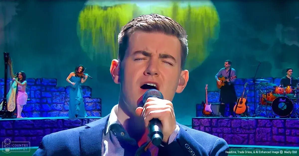 A young adult male singer performing on stage with a violinist, harpist, and guitarists in front of an abstract screen backdrop under colorful stage lights.