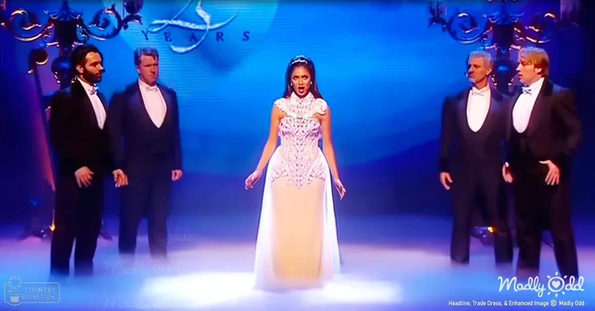 A young adult female performer in a white lace dress stands center stage at an indoor performance venue, flanked by two formally dressed male individuals wearing black tuxedos. The setting includes decorative lighting and a backdrop with 'YEARS' text.