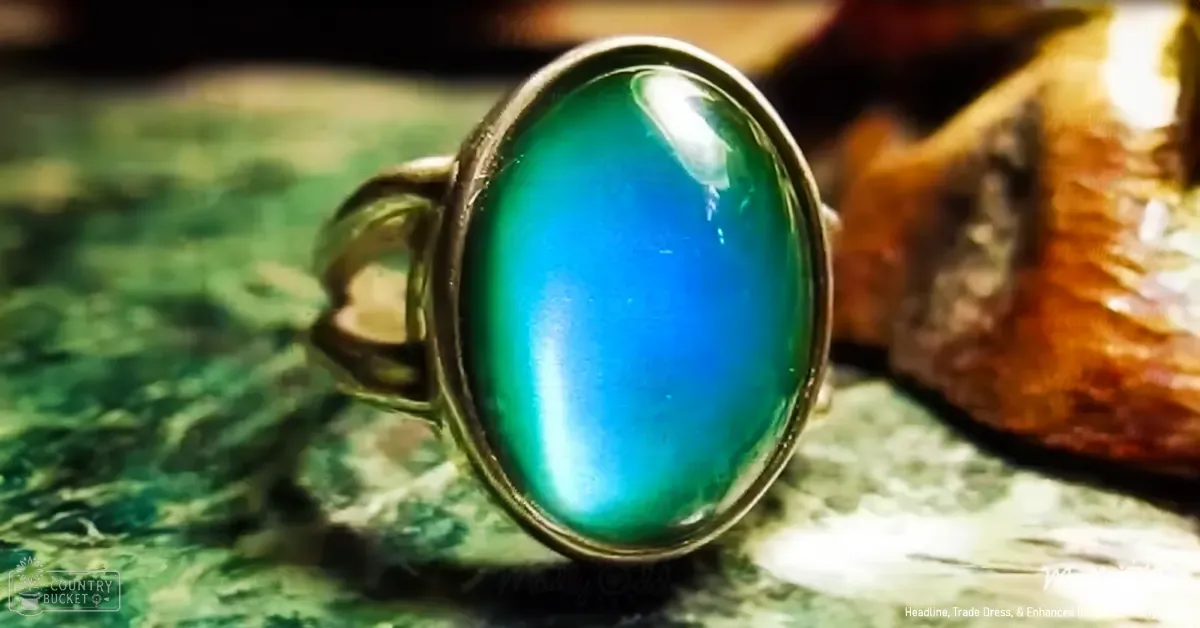 A studio setting showcasing a ring with an oval gemstone transitioning from green to blue, placed on a textured surface with shades of green and brown.