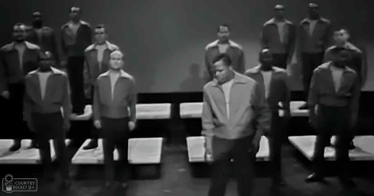 A group of adult males dressed uniformly in casual jackets and pants indoors, possibly at an event or performance.
