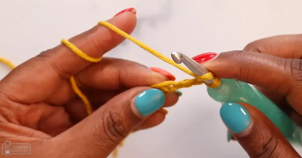 Close-up of hands engaged in crocheting, with a teal bracelet and yellow yarn as focal points against a plain white background.