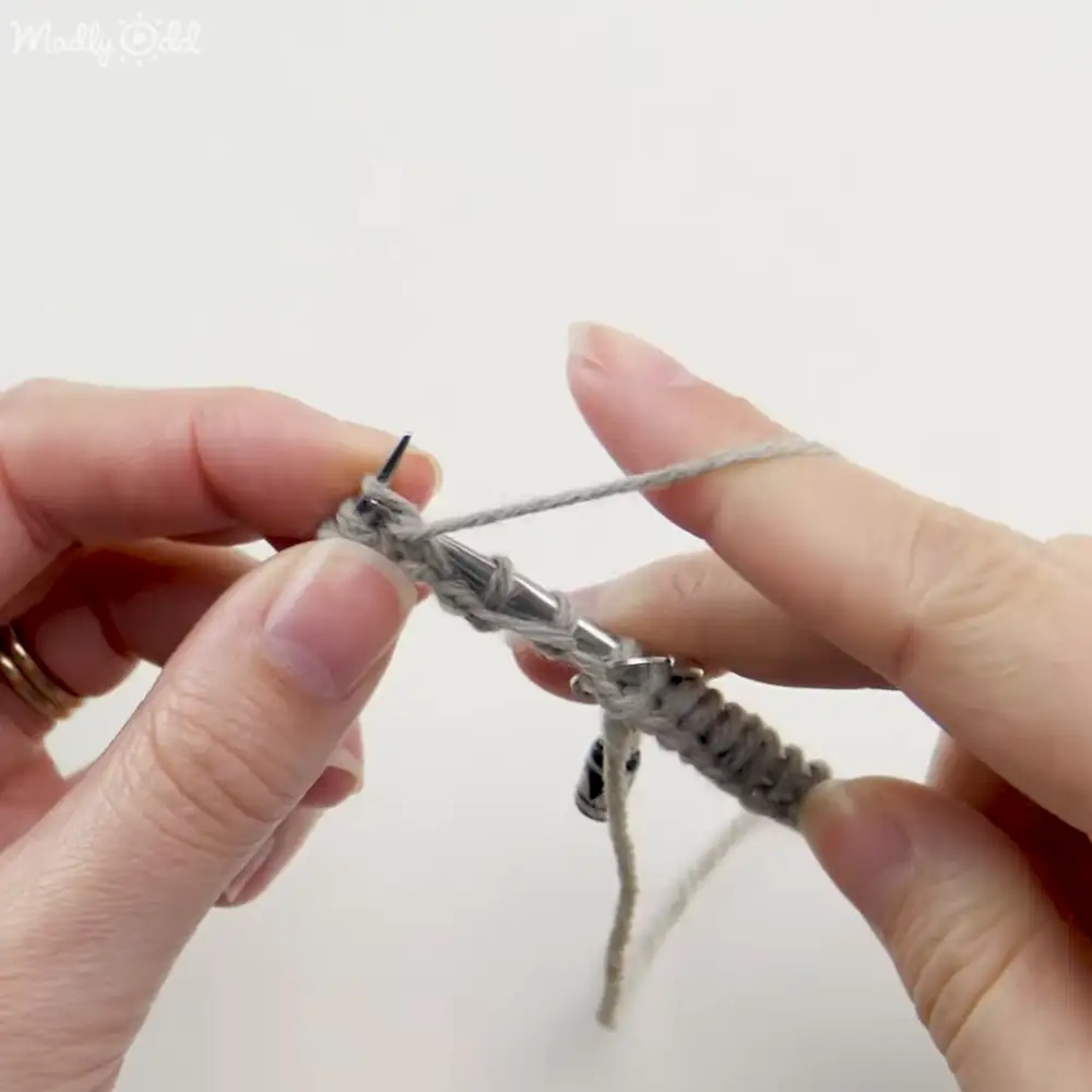 An adult female engaged in knitting with gray yarn on white background, focused on the activity in a controlled indoor setting.