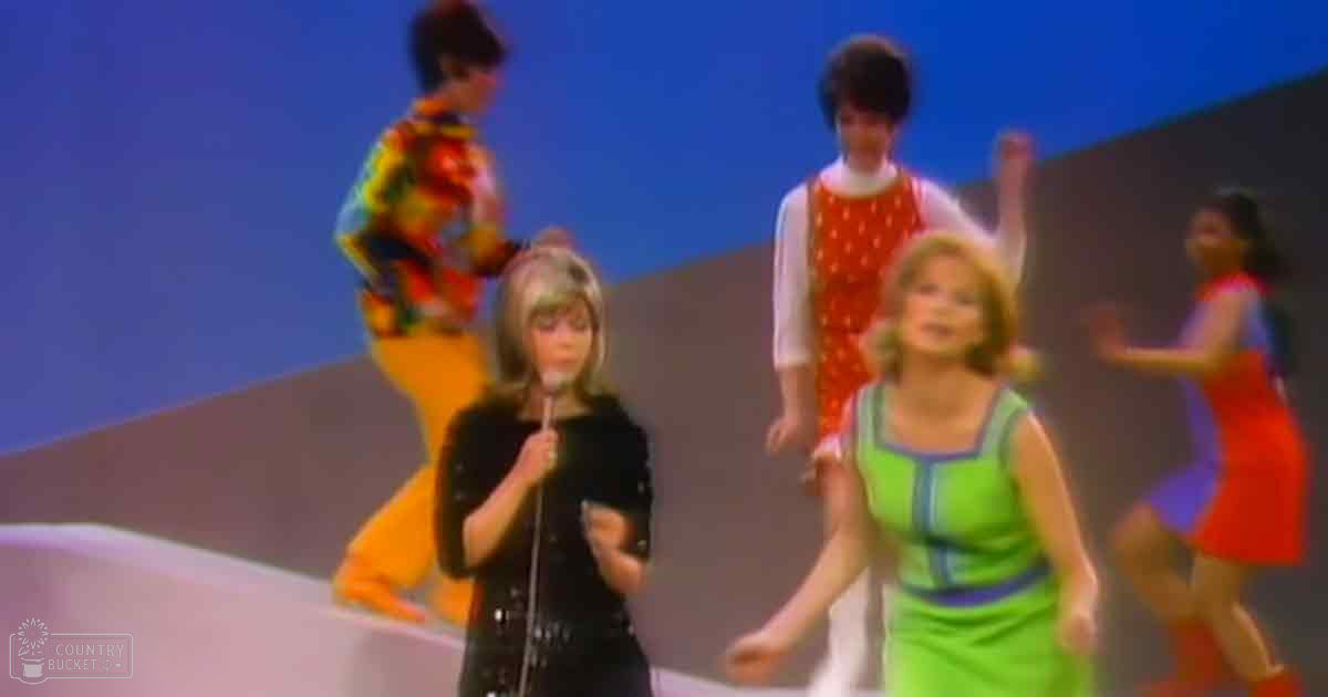 A group of performers on stage in a retro setting with blue and orange tones.