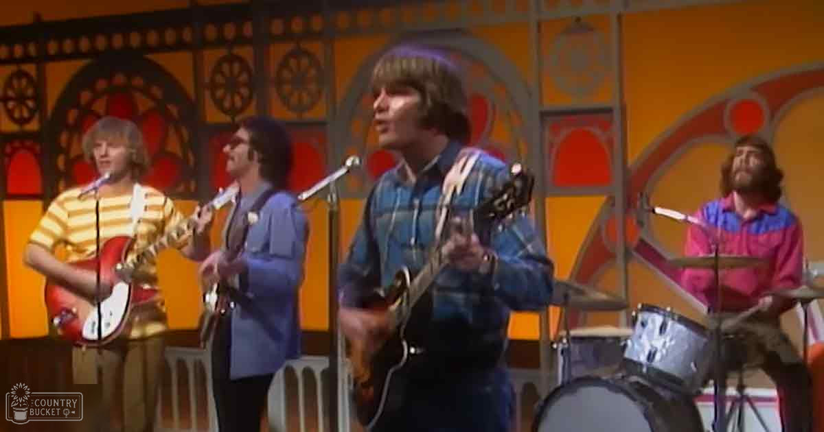 A vibrant musical performance with performers holding guitars, a mandolin/banjo player singing into a microphone, and a drummer; colorful ornate studio backdrop resembling exotic Middle Eastern or South Asian architecture.