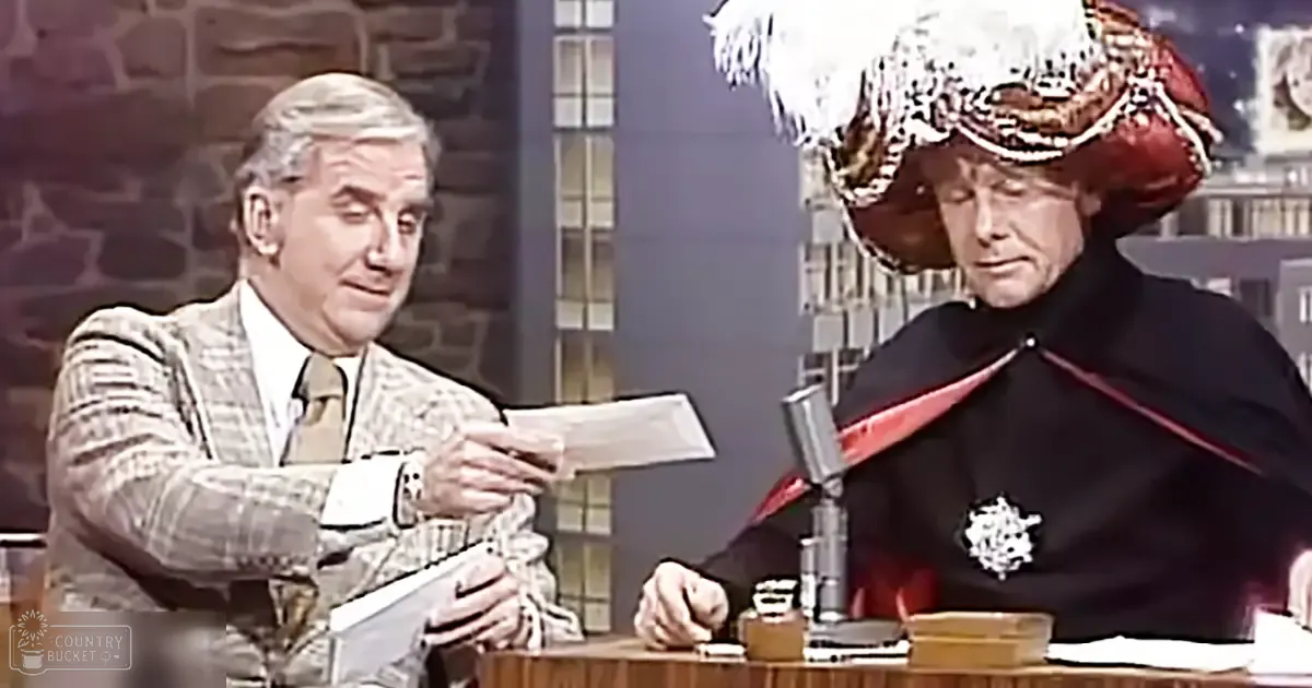 Two older adults engage in a comedic skit indoors, one dressed in a plaid blazer and another in a historical costume seated at a desk with a microphone.