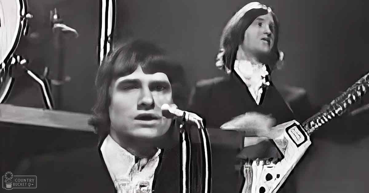 A musical performance scene with young adult males wearing formal outfits from the 1970s, with a drum set and microphone on stage at night.
