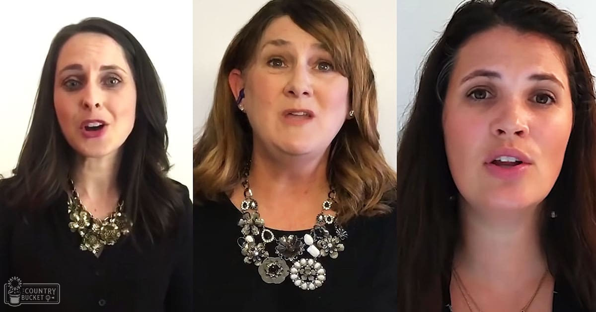 Three women wearing black tops with floral statement necklaces, set against a plain white background suggesting an indoor recording or photography studio environment.