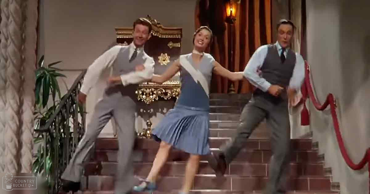 A dance sequence in an opulent indoor setting with ornate decor, grand staircase, and luxurious furnishings.