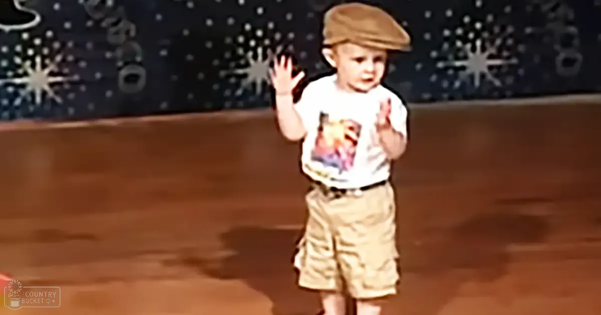 A toddler wearing a white t-shirt with 'Molly Dodd' printed on it, khaki shorts, and a brown cap sits against a dark backdrop with star-like patterns.