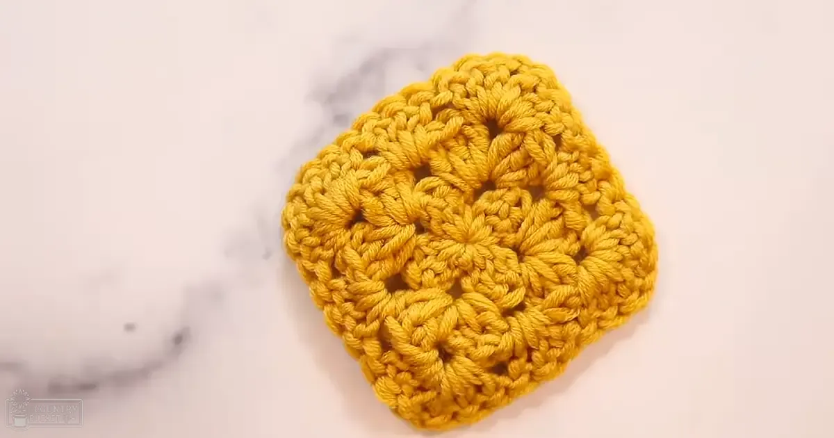 A crocheted yellow flower with intricate patterns on a plain white surface with subtle gray marbling, suggesting an indoor setting.