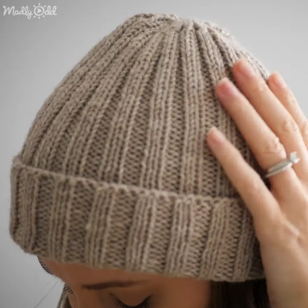 Adult female wearing a ribbed knit beanie with horizontal stripes indoors, ring visible on finger.