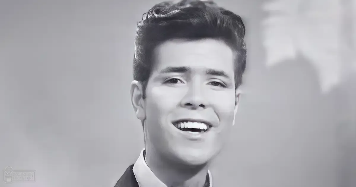 A young adult male wearing a white-collared shirt and dark jacket, set against a blurred urban backdrop with soft lighting.