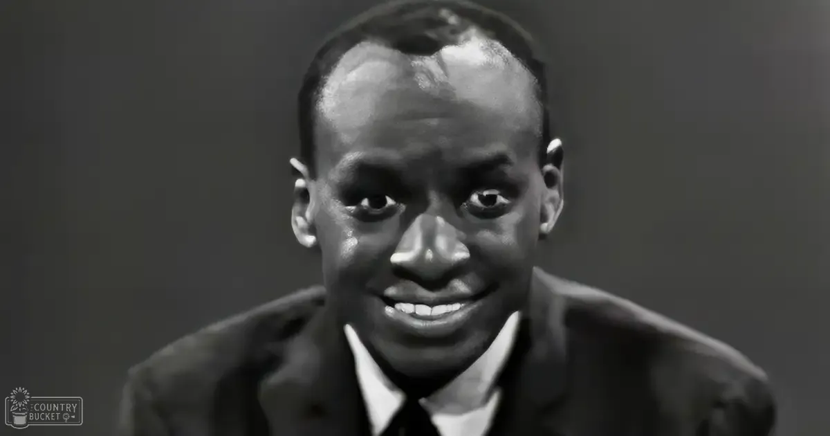 A young adult male wearing a tailored suit jacket over a collared dress shirt, set against a plain indoor background.