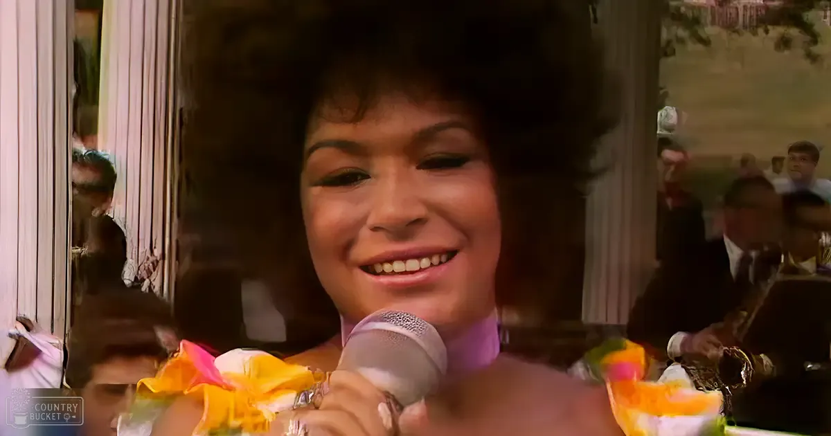 A female adult singer in a colorful floral outfit holds a microphone, likely performing at a restaurant or bar with natural light streaming through windows during spring or summer.