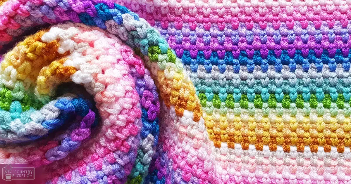 A close-up view of a colorful crocheted textile indoors with various stripes in shades of pink, purple, blue, green, yellow, orange, and white.