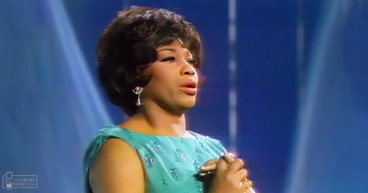 Adult female performer in a teal sequined dress, holding a microphone on stage with 'Madly Odd' text visible.