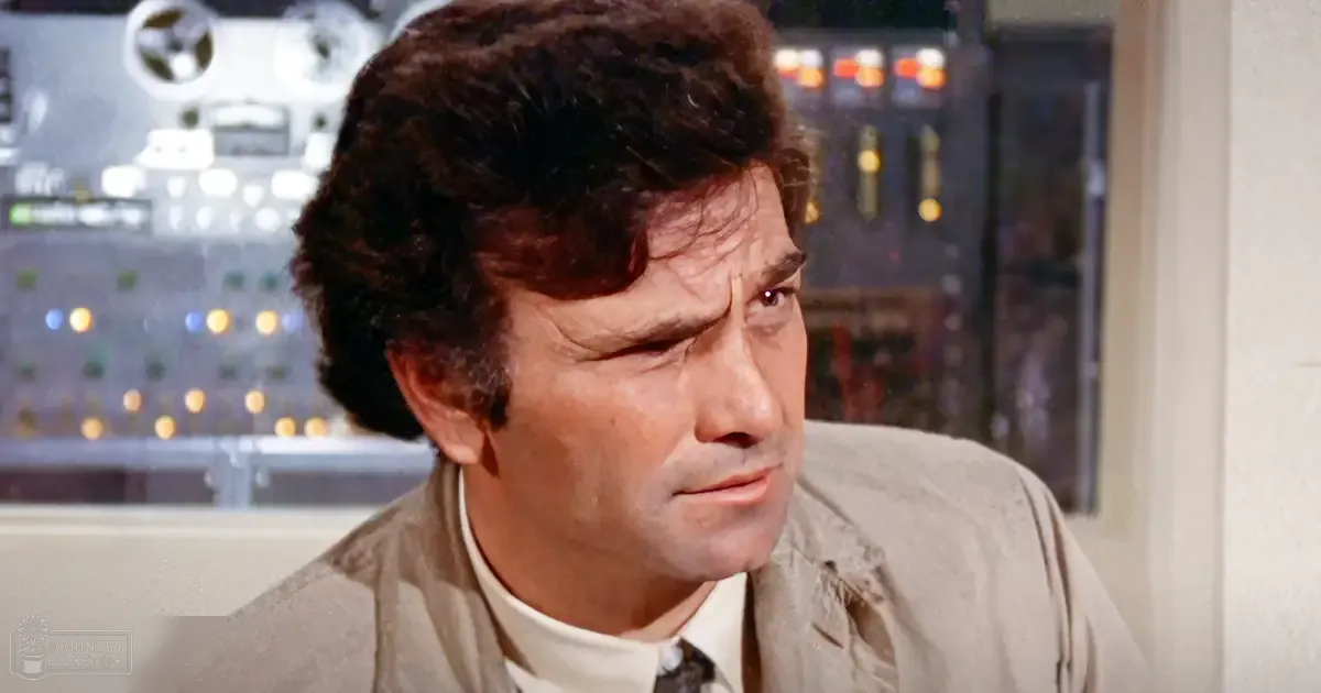 An adult male wearing a light-colored jacket in an indoor setting with artificial lighting.