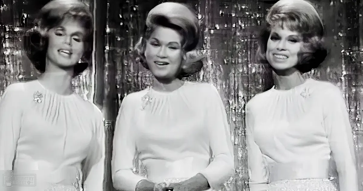 Group of women in mid-20th century dresses indoors with reflective curtains, likely daytime lighting.