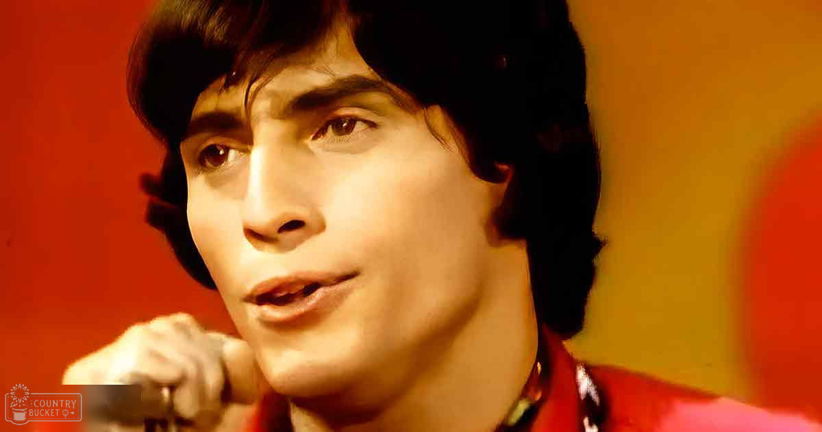 A young adult male in a relaxed fit red jacket with a collar and long sleeves, set against an indoor backdrop with warm color tones of red, yellow, and orange.