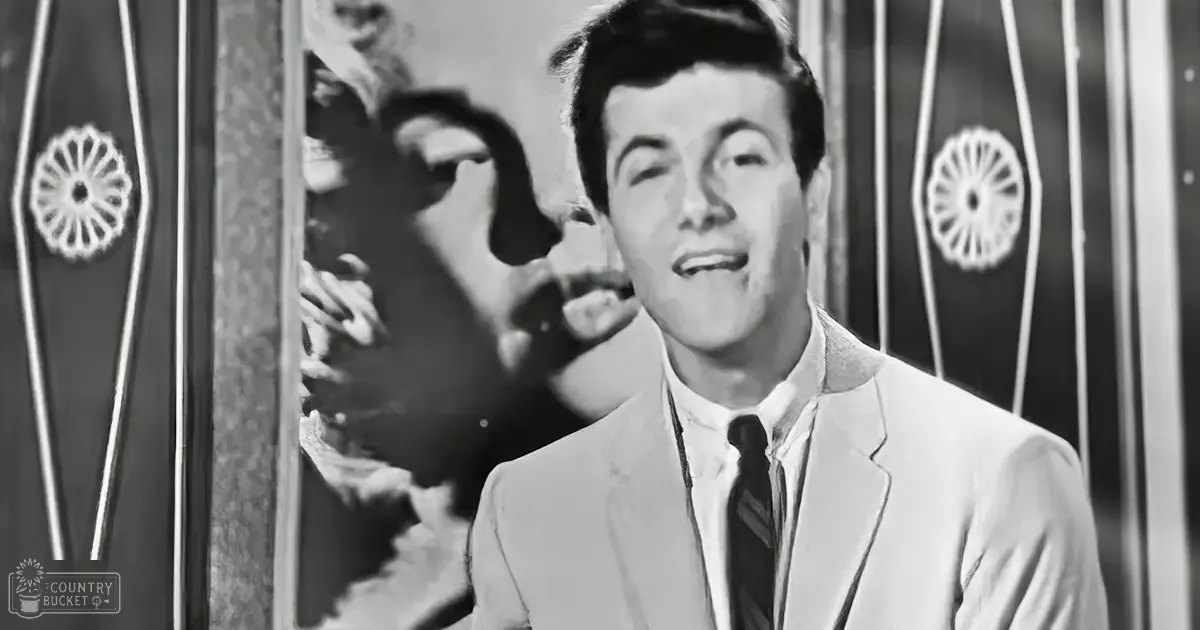 A young adult male in a light-colored suit jacket with a dark tie and white shirt, standing indoors, likely from the mid-20th century.