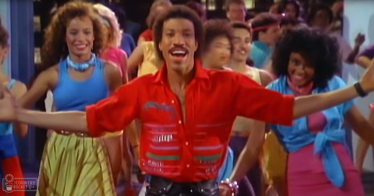 Adult male in a dance studio or performance space wearing a bright red button-up shirt with a graphic design; group of dancers in similar styles, vibrant colors typical of the 1970s fashion.