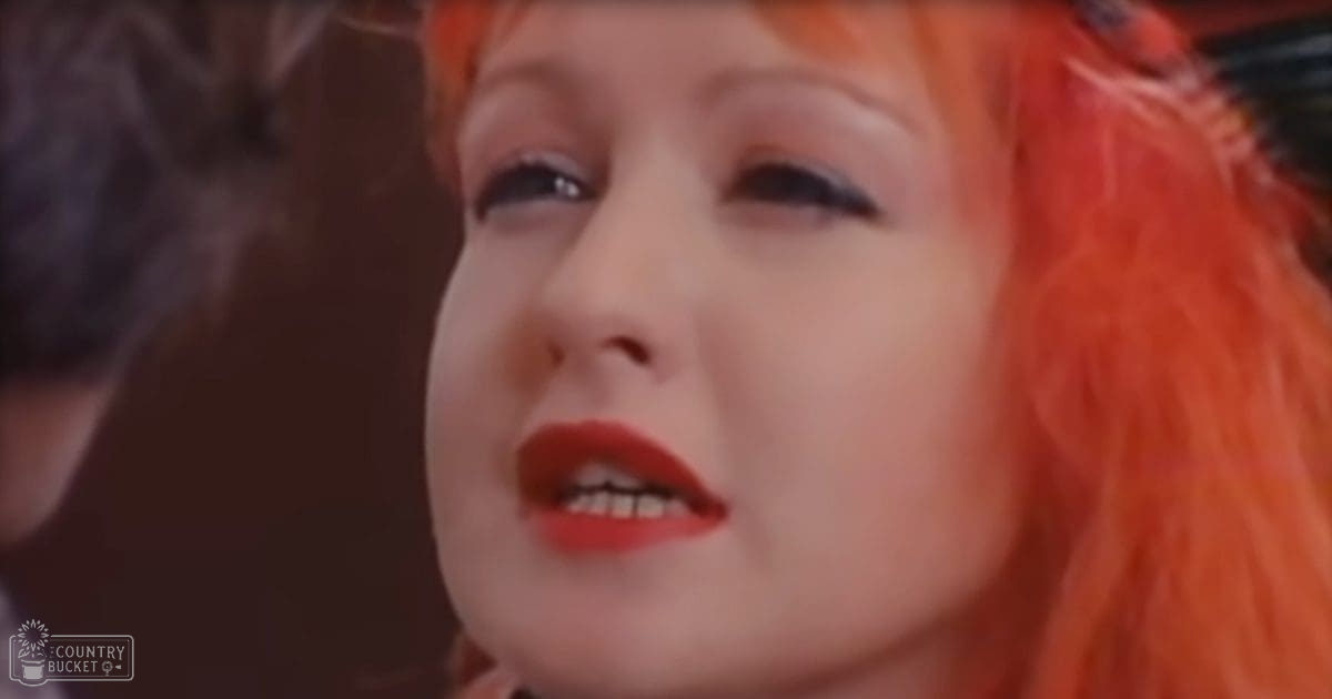 A young adult female with bright orange hair stands indoors against neutral-colored walls.
