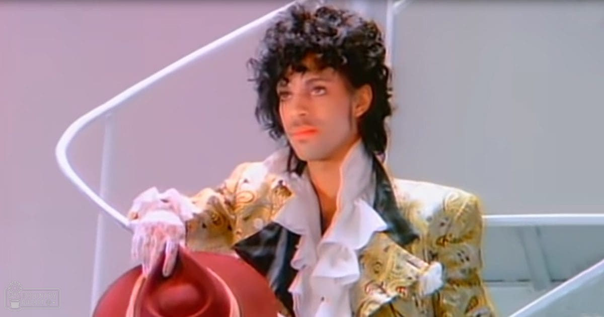A young adult male wearing a white ruffled collar shirt and black tie, accessorized with a red hat and white gloves, stands indoors against a plain light-colored wall.