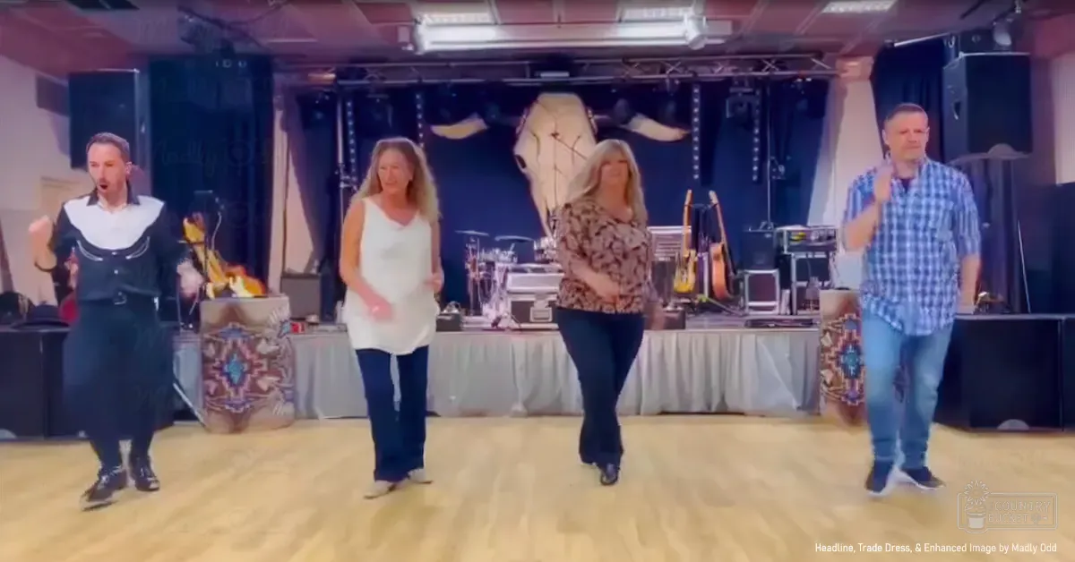An indoor dance hall scene with a group of adults dressed in traditional and casual attire, with wooden flooring and stage equipment including speakers and microphones; backdrop includes mounted cow head suggesting rural theme.