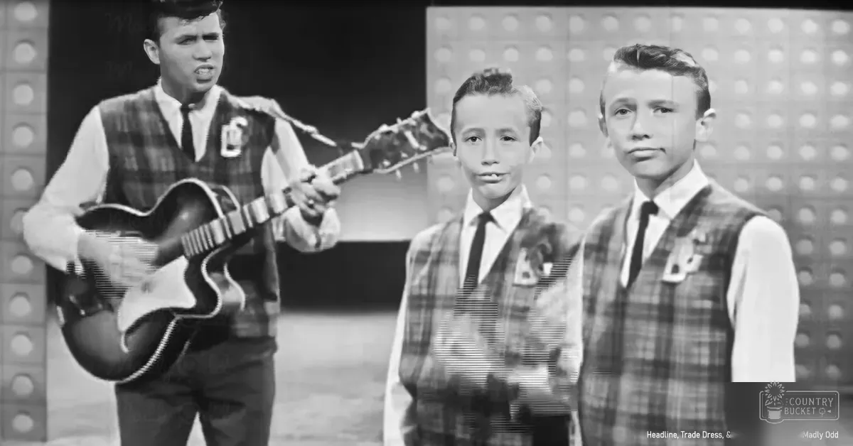 Child/teenage boys performing on an indoor stage with circular lights, grayscale setting suggesting a live performance space during daytime or evening.