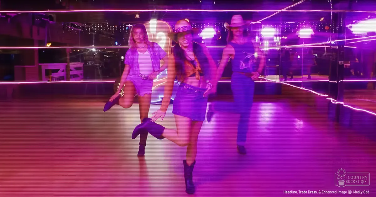 Dancers in a lively indoor setting, possibly a nightclub or dance hall; adult females wearing casual attire with denim elements, black ankle boots, and vibrant purple lighting creating a lively atmosphere.